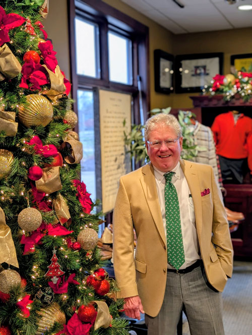 Man in suit standing next to Christmas tree